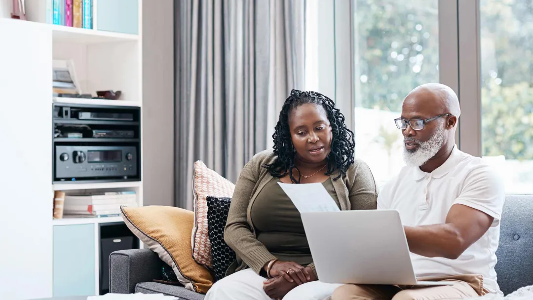 Man and woman reviewing paperwork with computer on lap