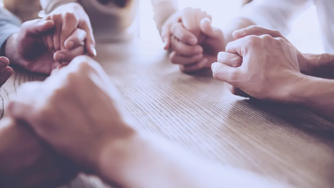 A group of friends holds hands in prayer.