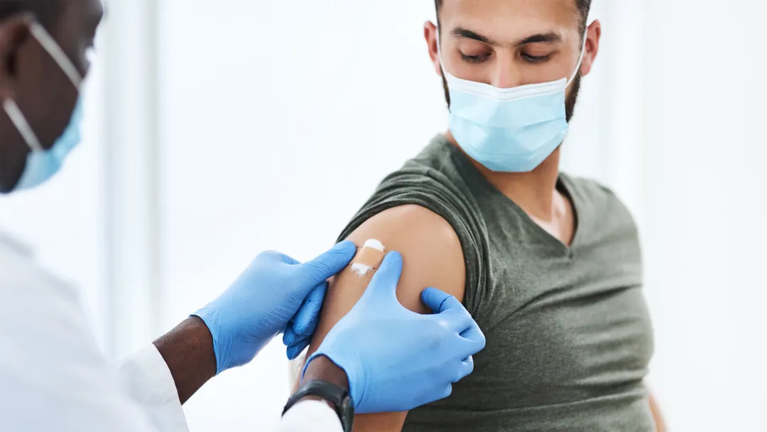 Man getting bandaged after a vaccine while wearing a mask.