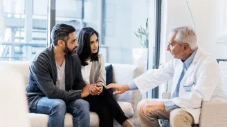 A couple, sitting with a doctor who is comforting them.