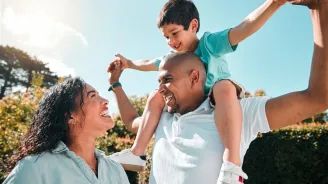 Dad lifting child on shoulders with mom smiling.