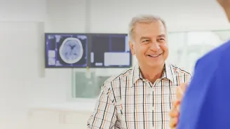 Man speaking with a doctor with imaging results on a screen behind him