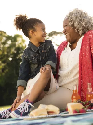 An African American granddaughter and grandmother sit outside for an evening picnic.