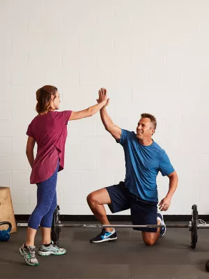 A Caucasian man and woman high-five while exercising at the gym.