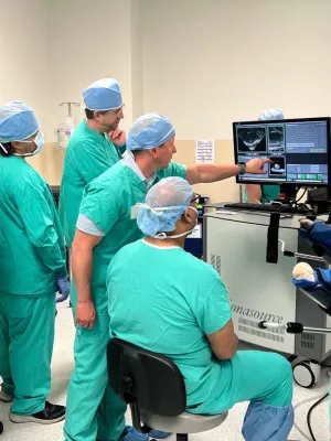 People in scrubs in operating room, pointing to screen.