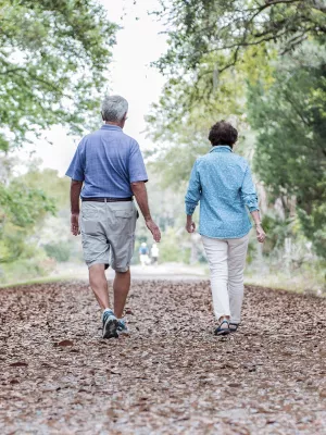 An elderly Caucasian couple takes an afternoon walk on a trail.