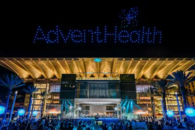 AdventHealth Orchestra performing at a night outdoor concert at Dr. Phillips Center for the Performing Arts with drones making the AdventHealth logo in the sky.