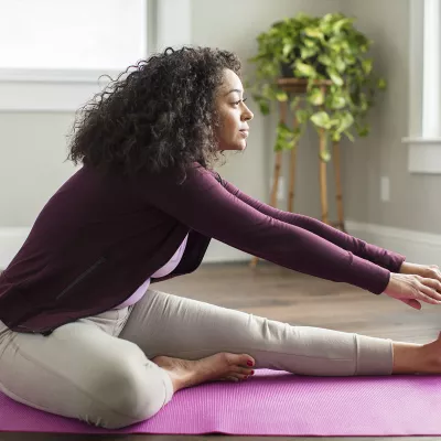 A young African American woman stretches for exercise in her living room.