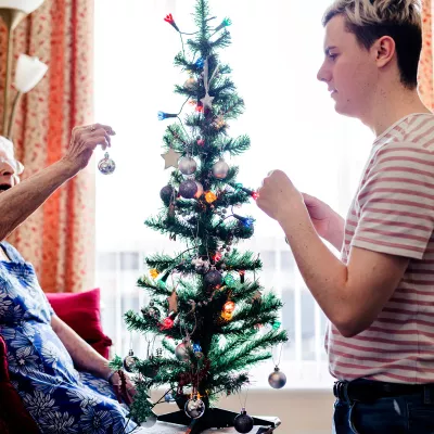 Grandmother dressing a Christmas tree with her young adult grandson
