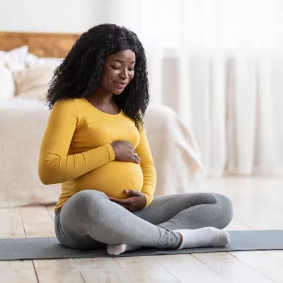 A Woman Sits on a Yoga Mat In Her Bedroom Embracing Her Pregnant Belly.