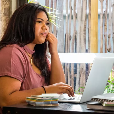 A Young Woman Sits at a Table and Surfs the Internet.
