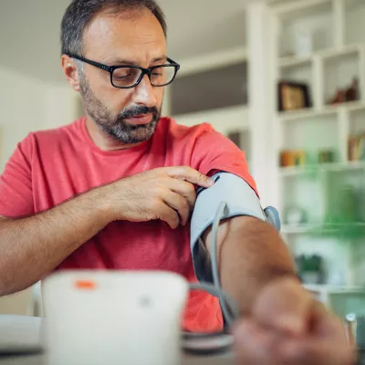 A Middle Aged Man Wearing Glasses Puts on a Blood Pressure Cuff to Take His Blood Pressure.