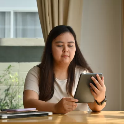 A Woman Reads a Tablet While Sitting at a Table at Home