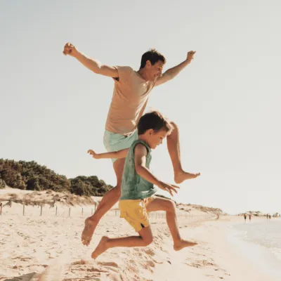 A Father and Son Jump Off a Dune on the Beach