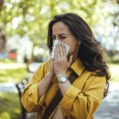 Woman blowing her nose into a tissue outdoors.
