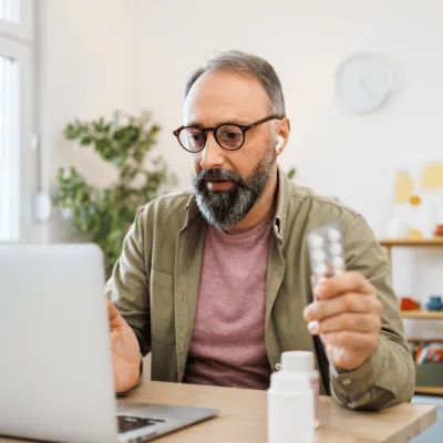 Man attending a virtual care appointment at home on laptop holding medication.