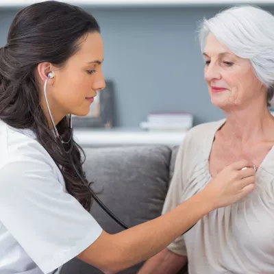A nurse checks a patient's heart beat as they are both sitting down.