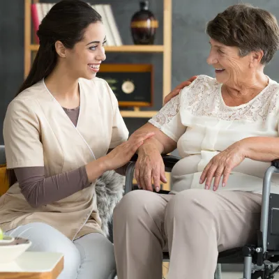 A woman in a wheelchair, with her caretaker sitting next to her and comforting her. Both are smiling.