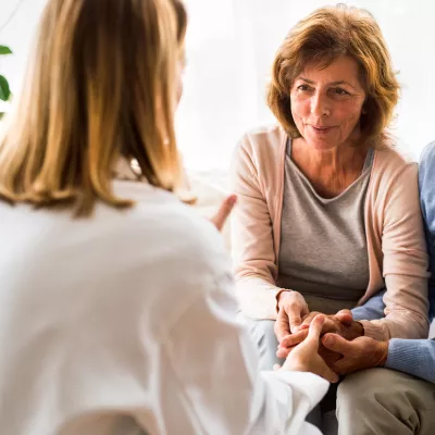 A senior couple, sitting down and holding hands, consulting a doctor at an appointment.