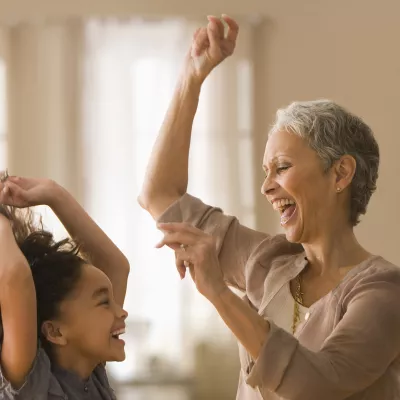 An elementary-aged girl and an older female relative dancing and smiling indoors