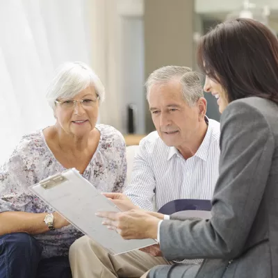 A female hospital staff member discusses information with an elderly couple.