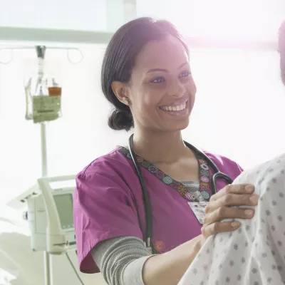 A female African American nurse consoles a woman in a hospital gown.