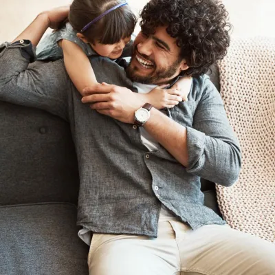 A daugther hugging her father who is sitting in the couch.