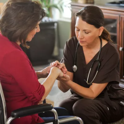 Woman in a wheelchair praying with a nurse.