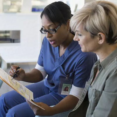 An African American nurse consults with a Caucasian female regarding her diagnosis.