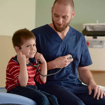 A male nurse lets his child patient listen to a stethoscope.