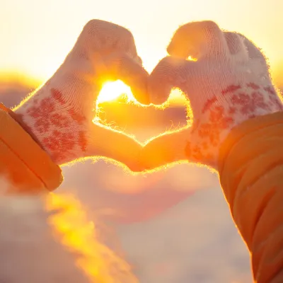 Woman in winter clothing making a heart with her hands.