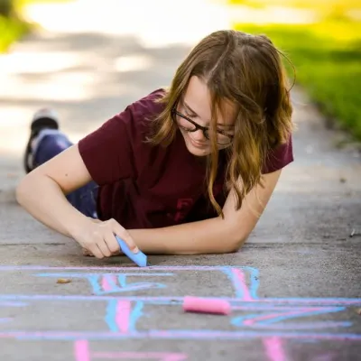 Girl chalks hopscotch game on sidewalk