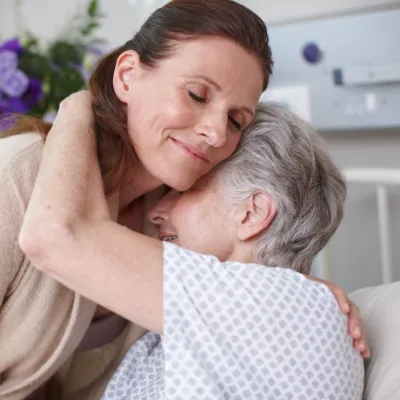 An adult daughter hugs her mom in the hospital.