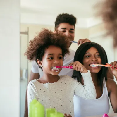 A young girl brushes her teeth with her parents as examples