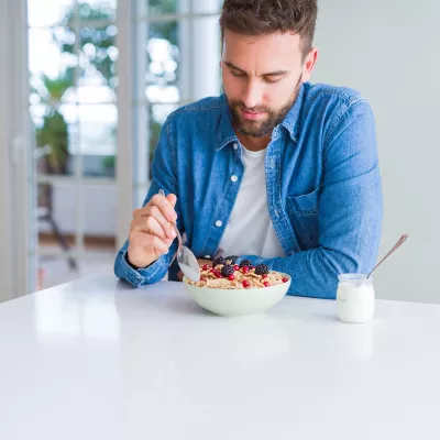 A gentleman eating a bowl of cereal with berries and a cup of yogurt
