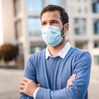 A man with his arms crossed standing outdoors wearing a mask.