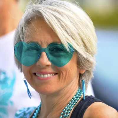 Anita Robinson, a woman with short blonde hair and tan skin, wearing teal heart-shaped sunglasses