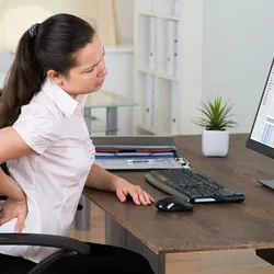 A woman puts her hand on her lower back while sitting.