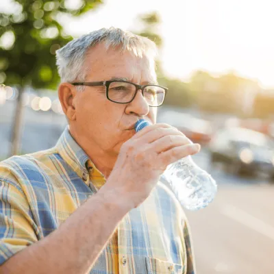 Older man drinking from a plastic water bottle.