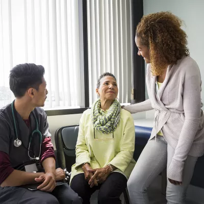 An African American daughter consoles her mother upon hearing medical news from the nurse.