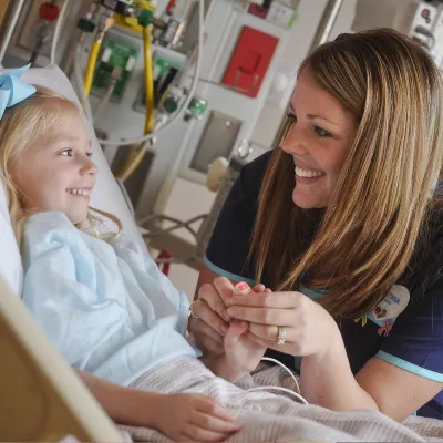 A female nurse consoles a young female patient in her hospital bed.