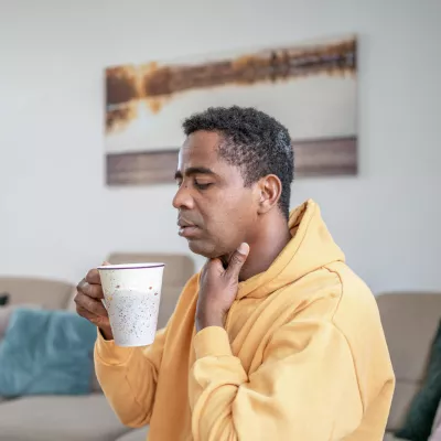 A man with a sore throat sips a cup of hot tea.