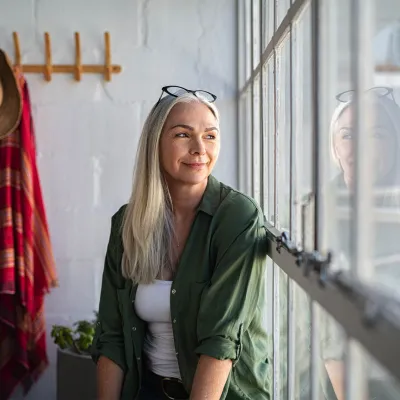 A mature woman sits at home and looks out a window