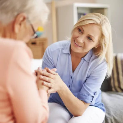 A middle-aged woman and her elderly mother hold hands.