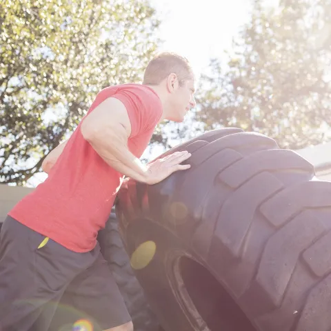 A young Caucasian man exercises outdoors by flipping large tires.