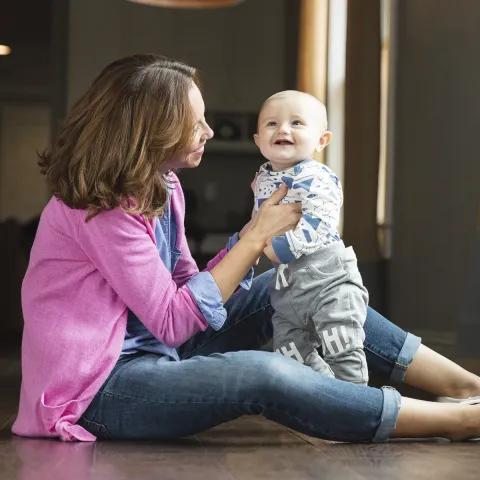 A young mother plays with her toddler on the floor.