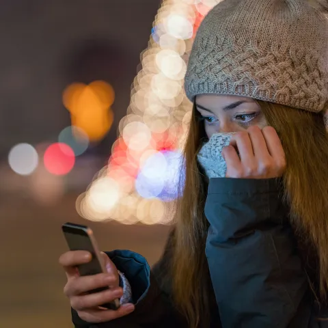 Woman outdoors bundled up in a beautiful winter's evening look at her cell phone