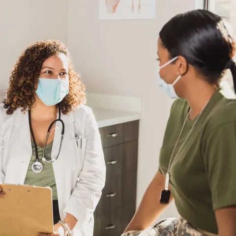 A Doctor Speaks to a Female Military Patient in an Exam Room.