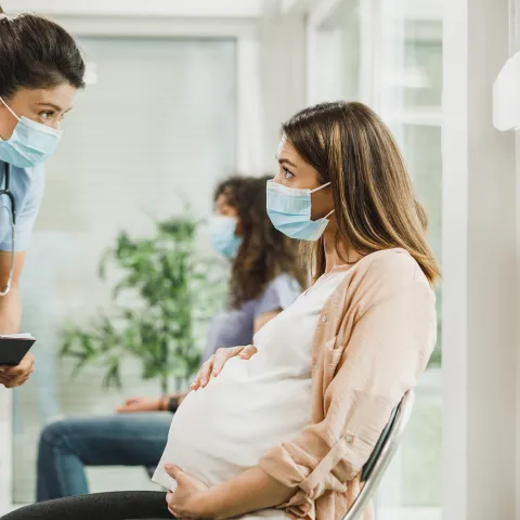 A Care Provider Speaks to a Patient While She Sits in the Waiting Room Holding Her Baby Bump.