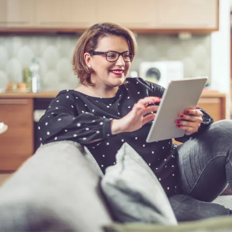 A Woman Smiles as She Looks at Content of Her Tablet at Home.